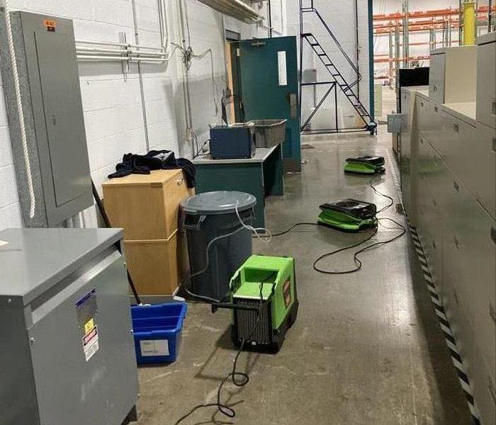 A dehumidifier and two air movers in an aisle with a dry floor in a warehouse