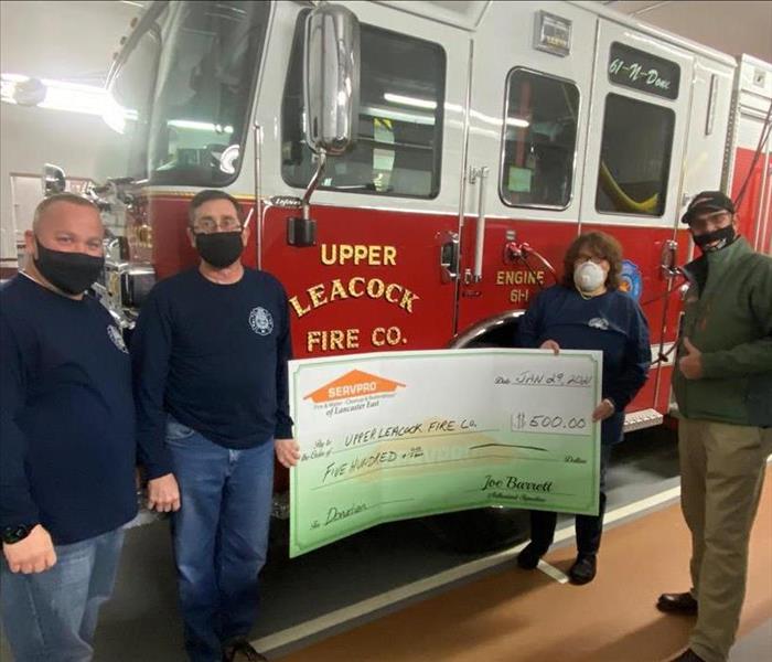 SERVPRO sales manager with members of a fire department holding a large check display board with a fire truck