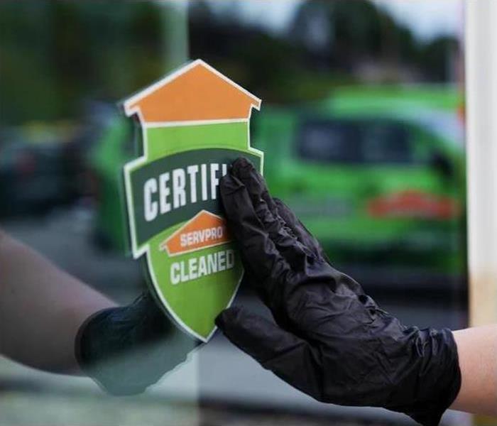 Hand with a latex glove on touching a Certified: SERVPRO Cleaned sticker on a window