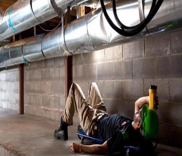  Technician laying down looking at an HVAC system with a flashlight
